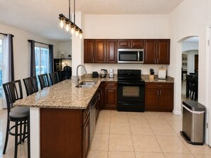 A kitchen with a central island, dark wooden cabinets, stainless steel appliances, and a hanging light fixture.