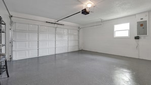 A clean, empty garage with a white garage door, a ceiling-mounted projector, and a window on the right wall.