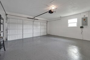 Eine saubere, leere Garage mit einer weißen Garagentür, einem an der Decke befestigten Projektor und einem Fenster an der rechten Wand.