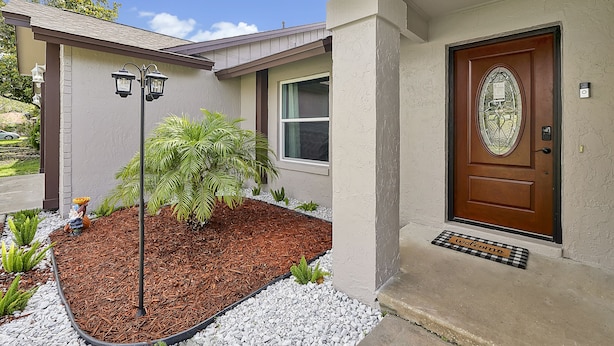A house with a brown door, a welcome mat, a small garden with plants, and a street lamp.