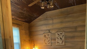 Une chambre confortable, aménagée dans un chalet en bois, avec un grand lit, une fenêtre et des illustrations d’oiseaux accrochées au mur.