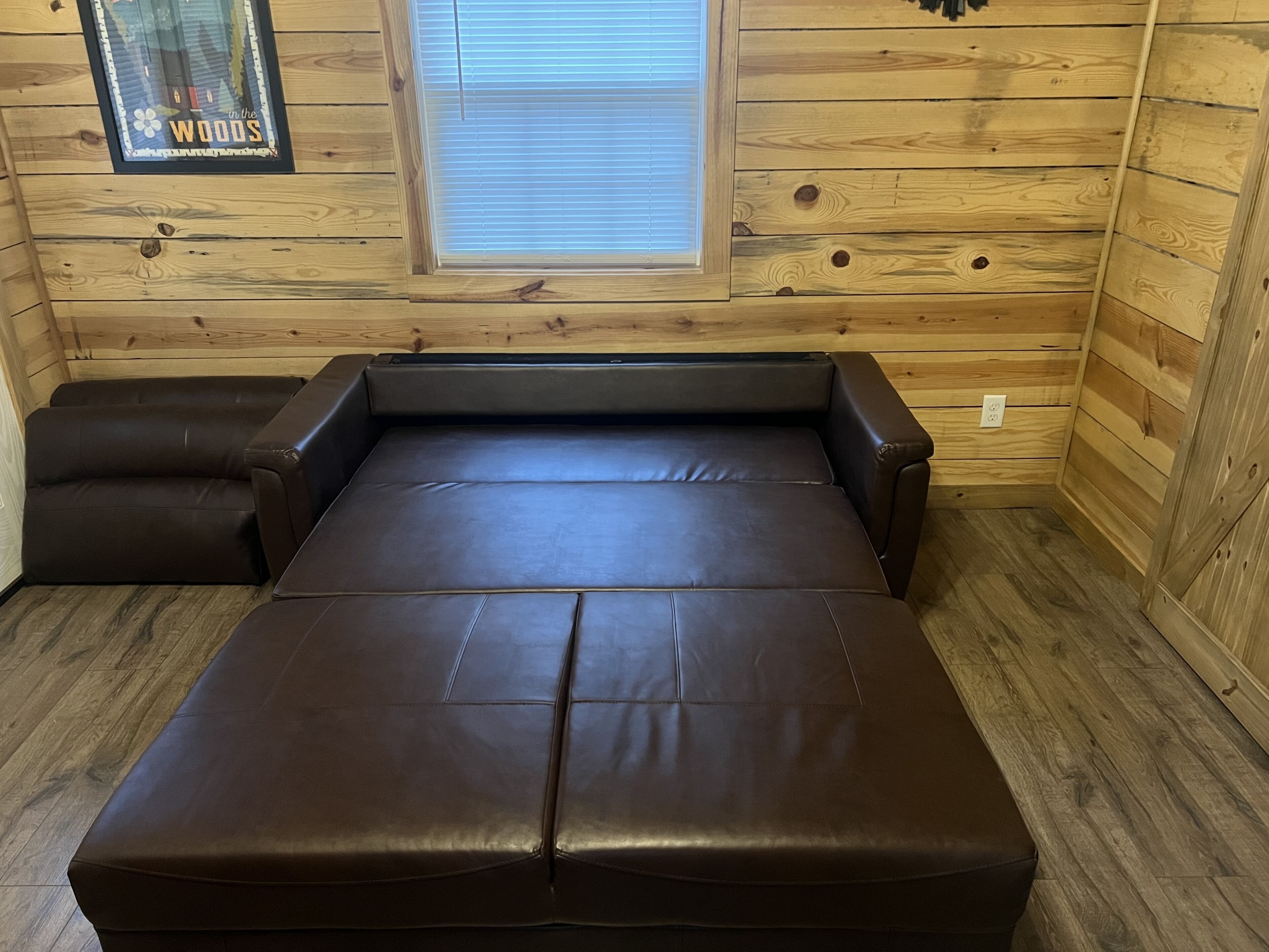 A wooden cabin room with a large bed, a window, and a framed picture on the wall.