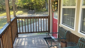 Une véranda en bois avec une balustrade, une porte rouge et deux chaises en métal avec un siège en osier tressé.