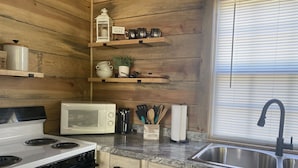 Une cuisine avec des murs en bois, un four blanc, un four à micro-ondes, un évier et des étagères remplies d’ustensiles de cuisine.