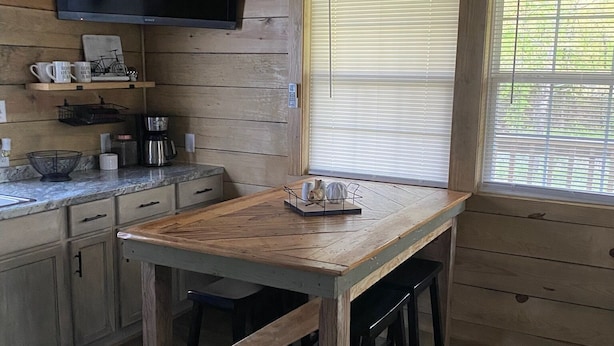 Une cuisine rustique aménagée dans une cabane en bois, avec une table, des chaises, une machine à café et un téléviseur fixé au mur.