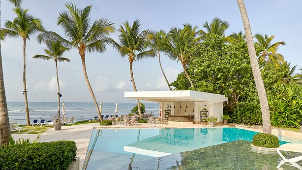 A pool area with clear blue water, surrounded by palm trees and a view of the ocean. - Caribbean Sea Panoramic View Suite on 17 Level (Playa Juan Dolio)
