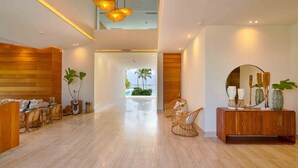 A modern lobby with a wooden reception desk, wicker chairs, a wooden console table with decorative items, and a view of the outdoors. - Caribbean Sea Panoramic View Suite on 17 Level (Playa Juan Dolio)