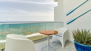 A balcony with a view of the sea, a round wooden table, white wicker chairs, and a large blue planter. - Caribbean Sea Panoramic View Suite on 17 Level (Playa Juan Dolio)