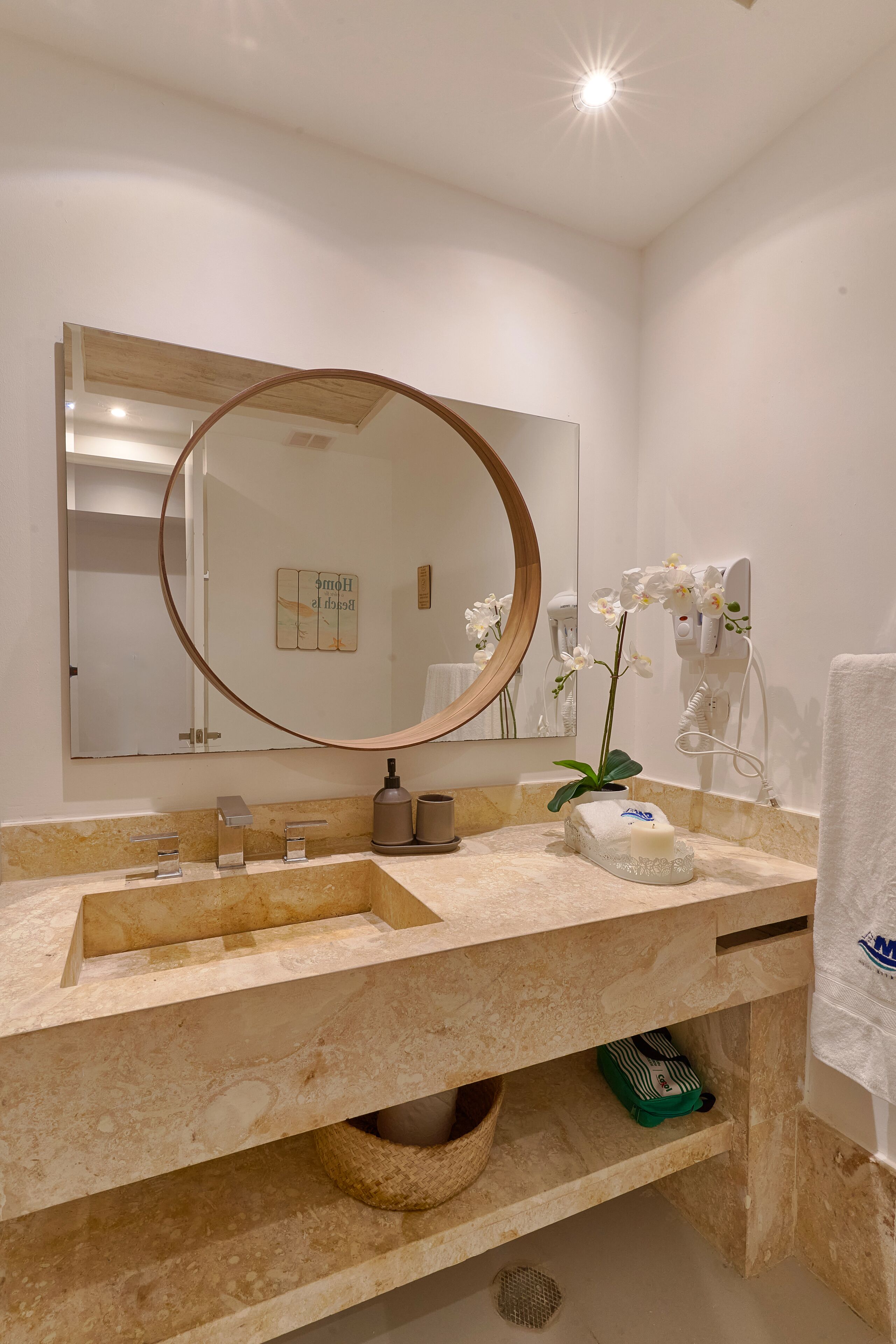 Un bagno con uno specchio grande, un lavandino, un portascopevoli e un asciugacapelli.