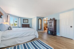 Ein Schlafzimmer mit einem großen Bett, einer Holzkommode, einem Spiegel und einer Tür zu einem weiteren Raum.