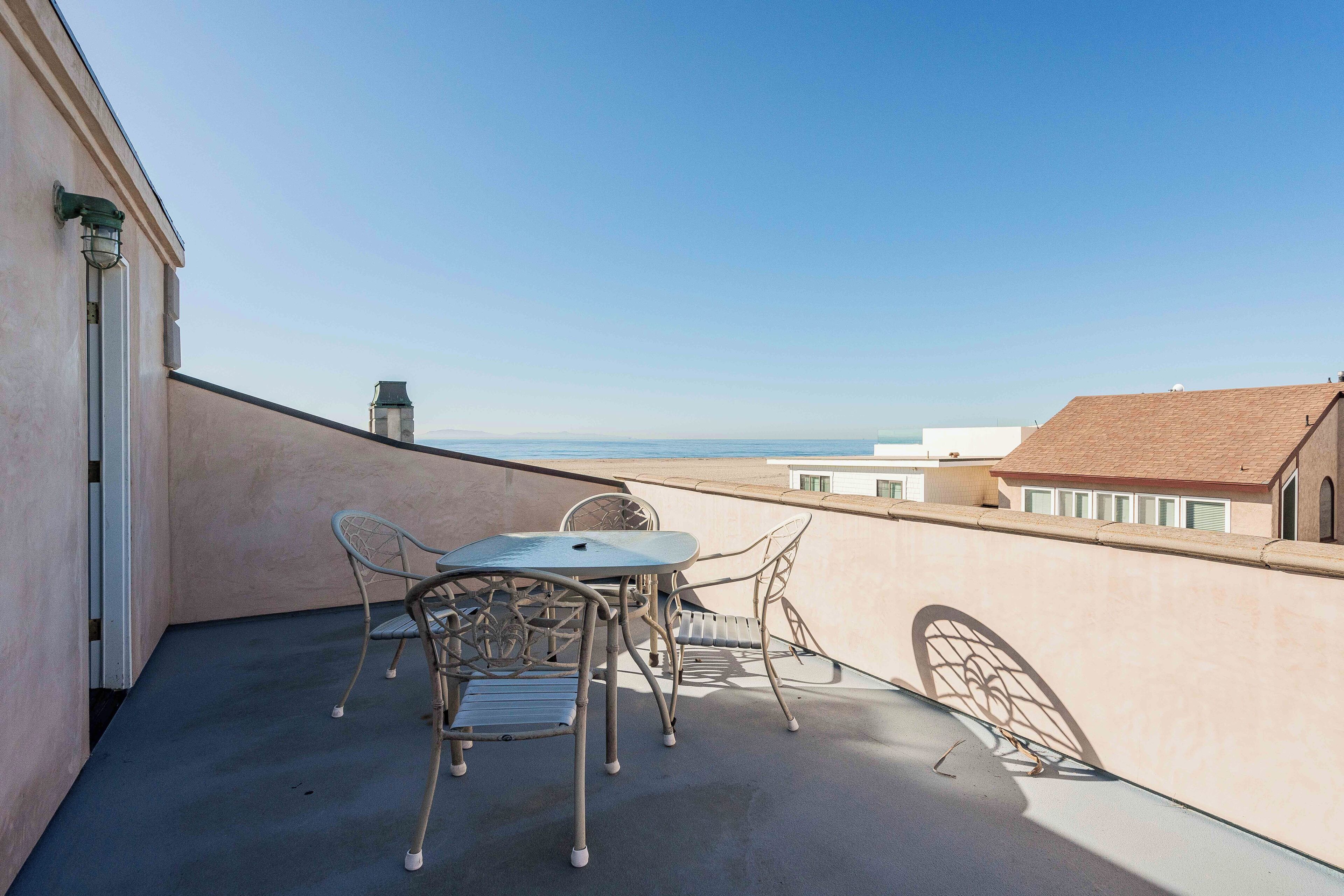 A balcony with a table and chairs, overlooking a cityscape and the sea.