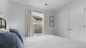 Une chambre avec un grand lit, une fenêtre avec des rideaux, une armoire et deux tableaux encadrés accrochés au mur.