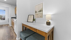 Une cuisine moderne avec des meubles blancs, un plan de travail en bois et un banc. On y trouve un panneau d’accueil encadré et une lampe posée sur le plan de travail.