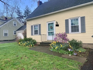 A two-story house with a front porch, a garage, and a well-maintained garden with daffodils and other flowers.