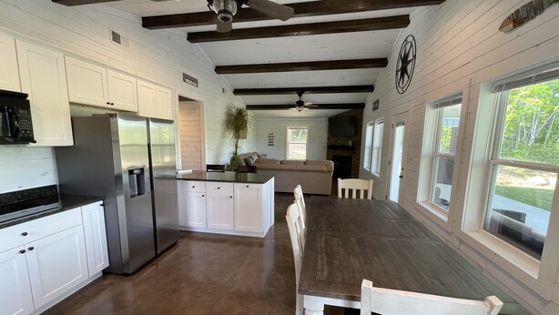 A spacious kitchen with white cabinets, a stainless steel refrigerator, and a dining area with a wooden table and white chairs. - 4 Bedroom 3 Bath Lakefront Home with Private Dock, Secluded, Lewis Smith Lake (Double Springs)