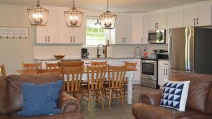 A modern kitchen with white cabinets, a stainless steel refrigerator, and a dining area with wooden chairs and a brown leather couch. - Gainesboro, TN House, Dale Hollow Lake, Standing Stone State Park, Roaring River (Gainesboro)