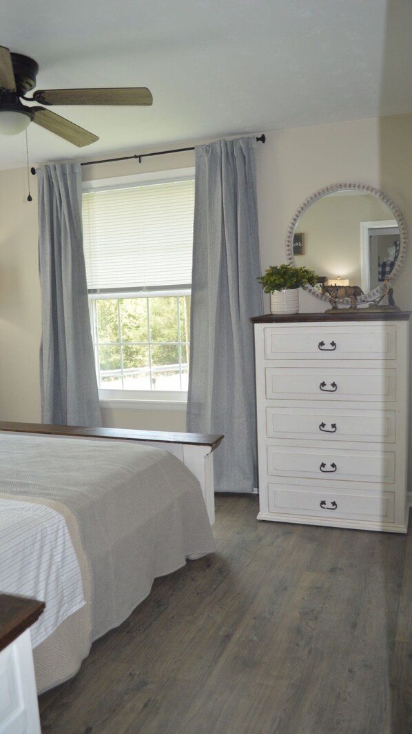 A bedroom with a bed, a dresser, a ceiling fan, and a window with curtains.
