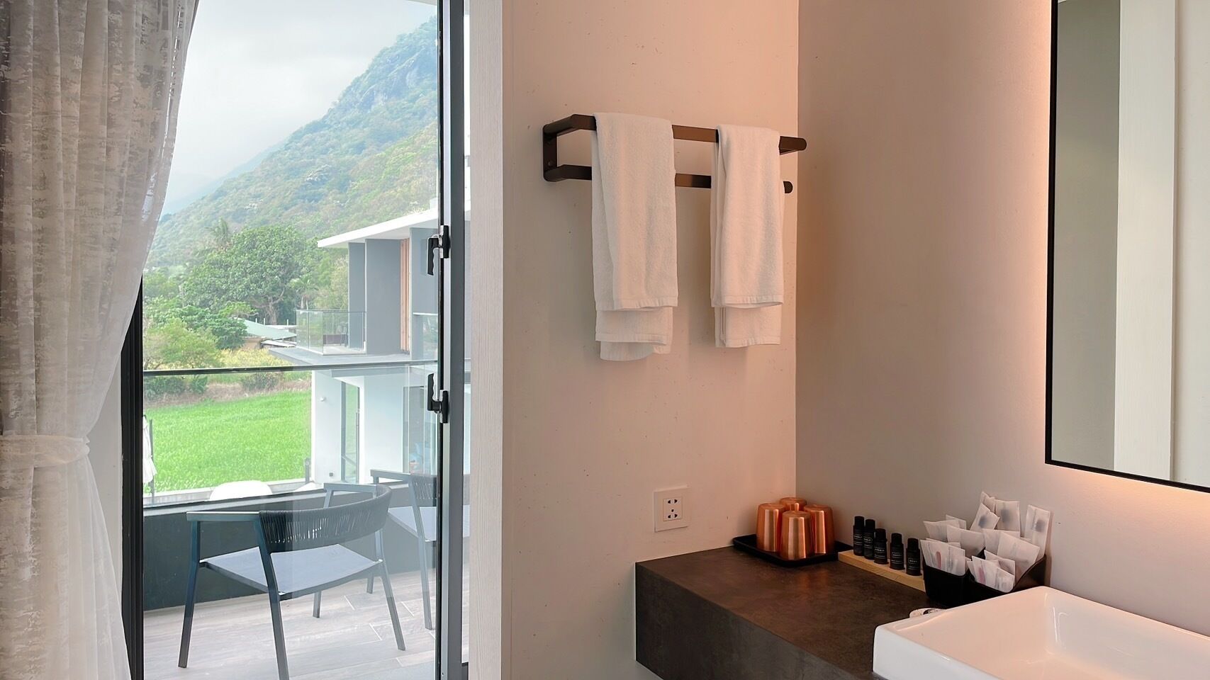 Un baño moderno con un espejo grande, un lavabo y un ventanal con vistas a un balcón.