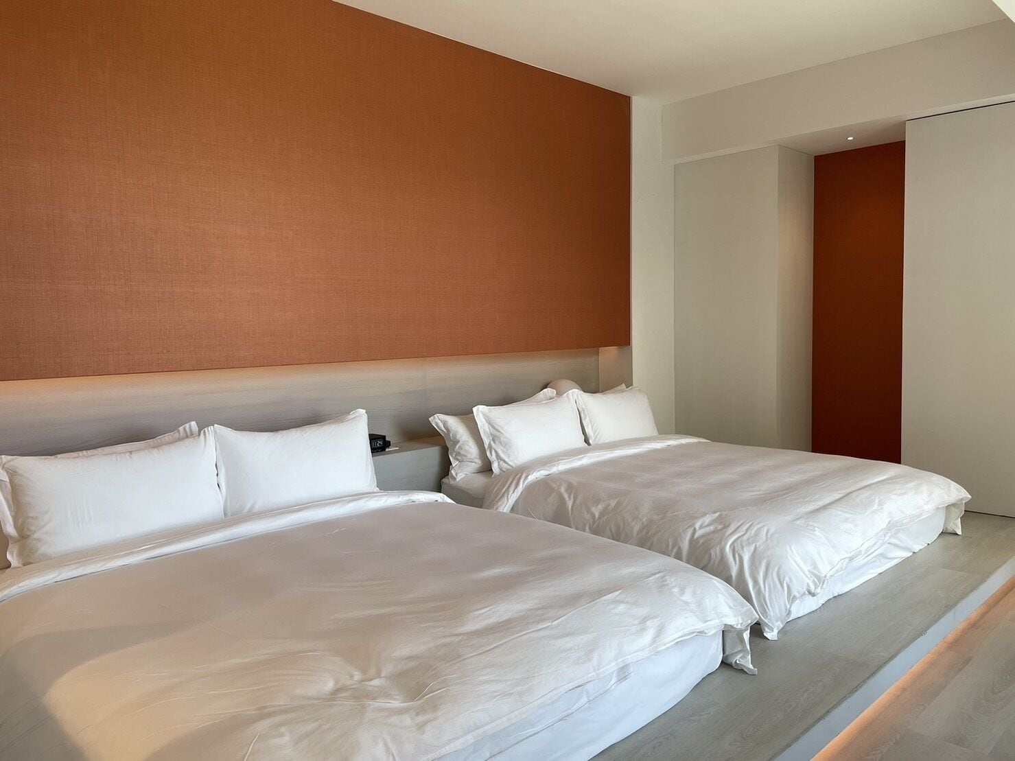 Habitación de hotel con dos camas, cabecero de madera y una paleta de colores neutros.