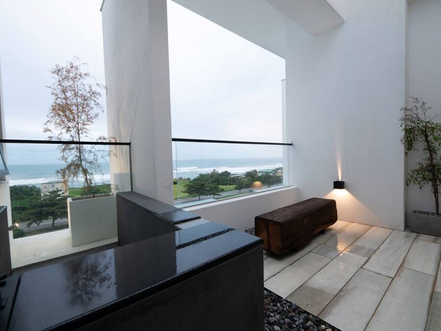 A modern balcony with a view of the ocean, a bench, and a wall-mounted light fixture.