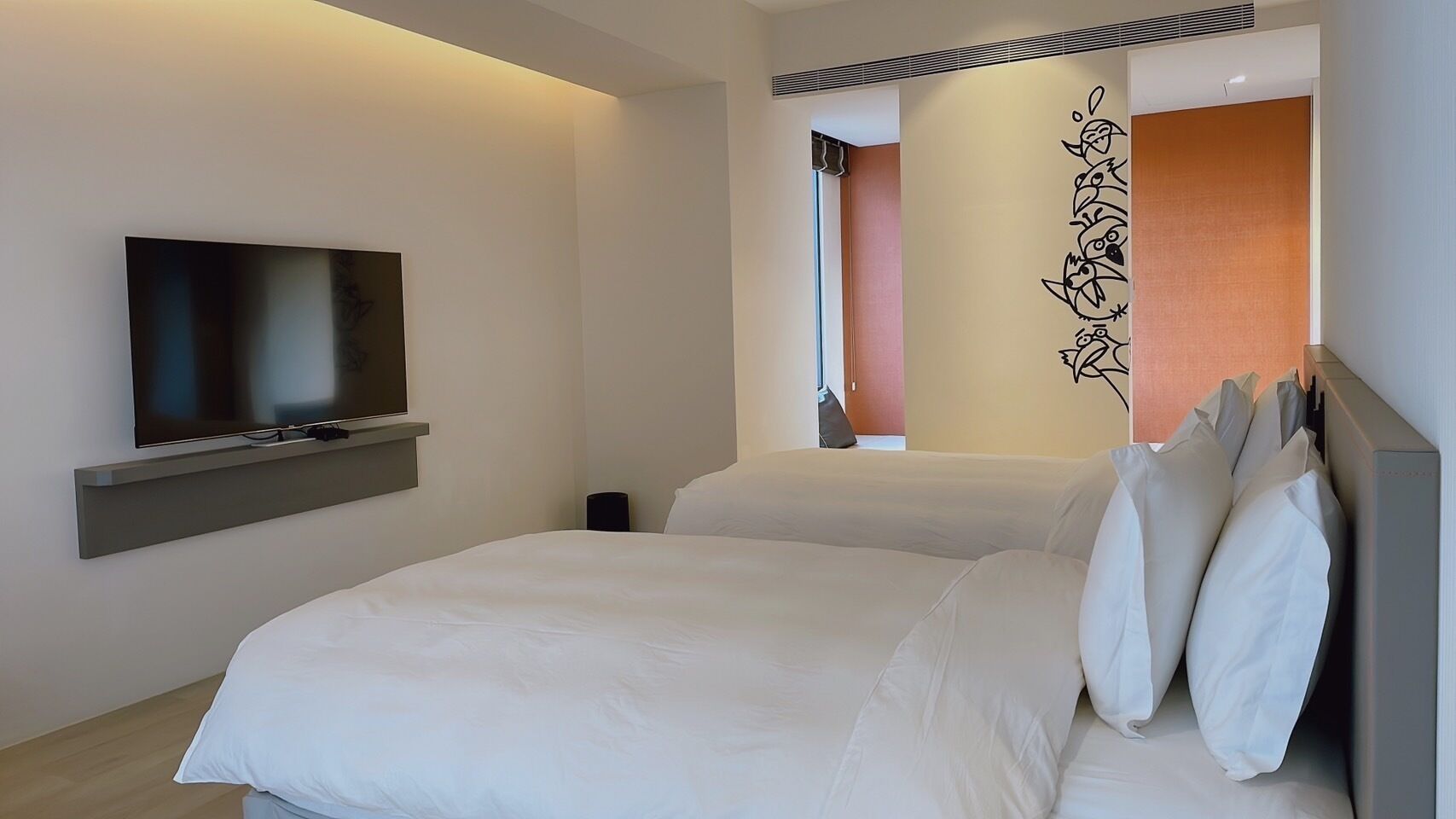 A modern hotel room with a large bed, a flat-screen TV mounted on the wall, and a decorative wall piece.