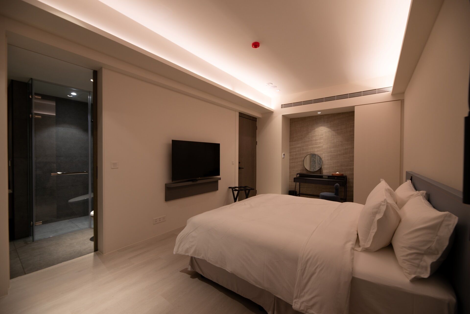 A modern hotel room with a large bed, a flat-screen TV mounted on the wall, a small table with a mirror, and a walk-in closet.
