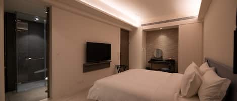 A modern hotel room with a large bed, a flat-screen TV mounted on the wall, a small table with a mirror, and a walk-in closet.