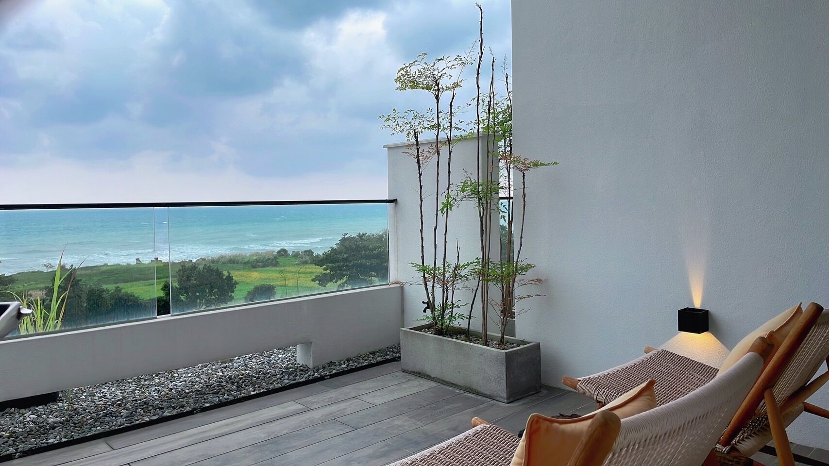 A balcony with a view of the ocean, a seating area with cushions, and a potted plant.
