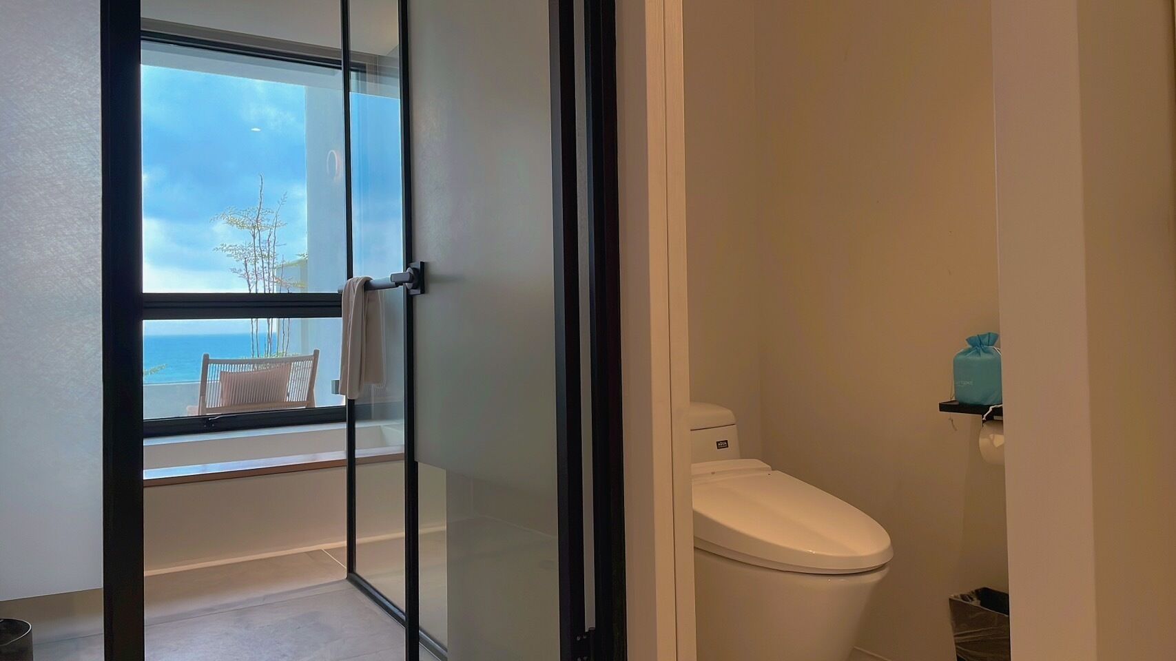 A bathroom with a toilet, a window, and a view of the sea.