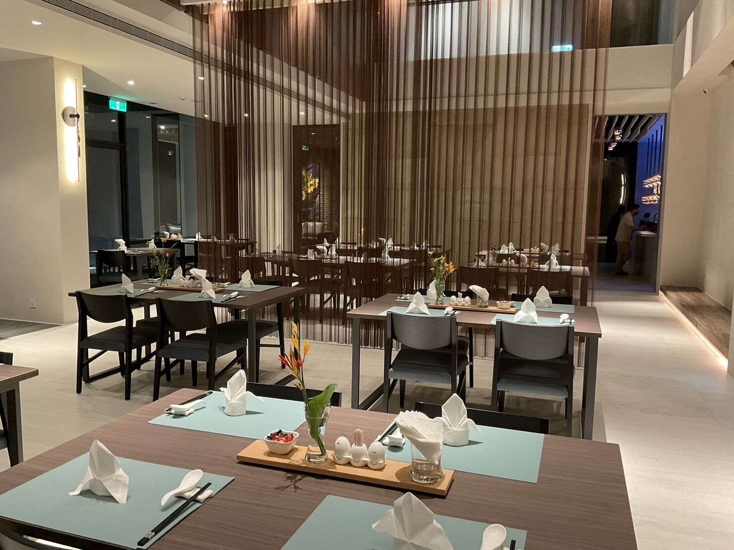 A modern dining area with multiple tables and chairs, some with napkins and cutlery.
