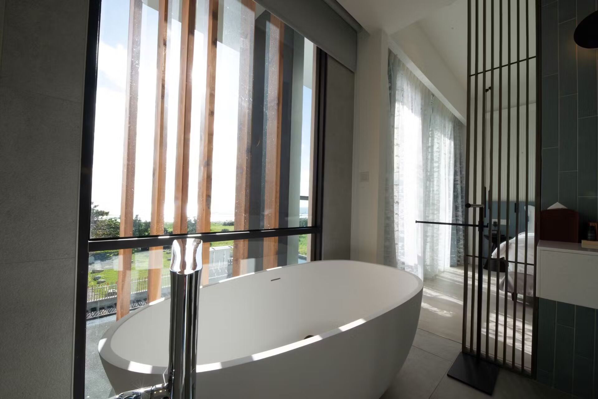 A modern bathroom with a freestanding bathtub, large windows, and a view of greenery outside.