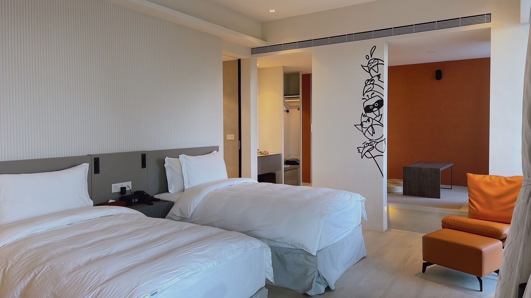 A hotel room with two beds, a desk, a chair, and a decorative wall.