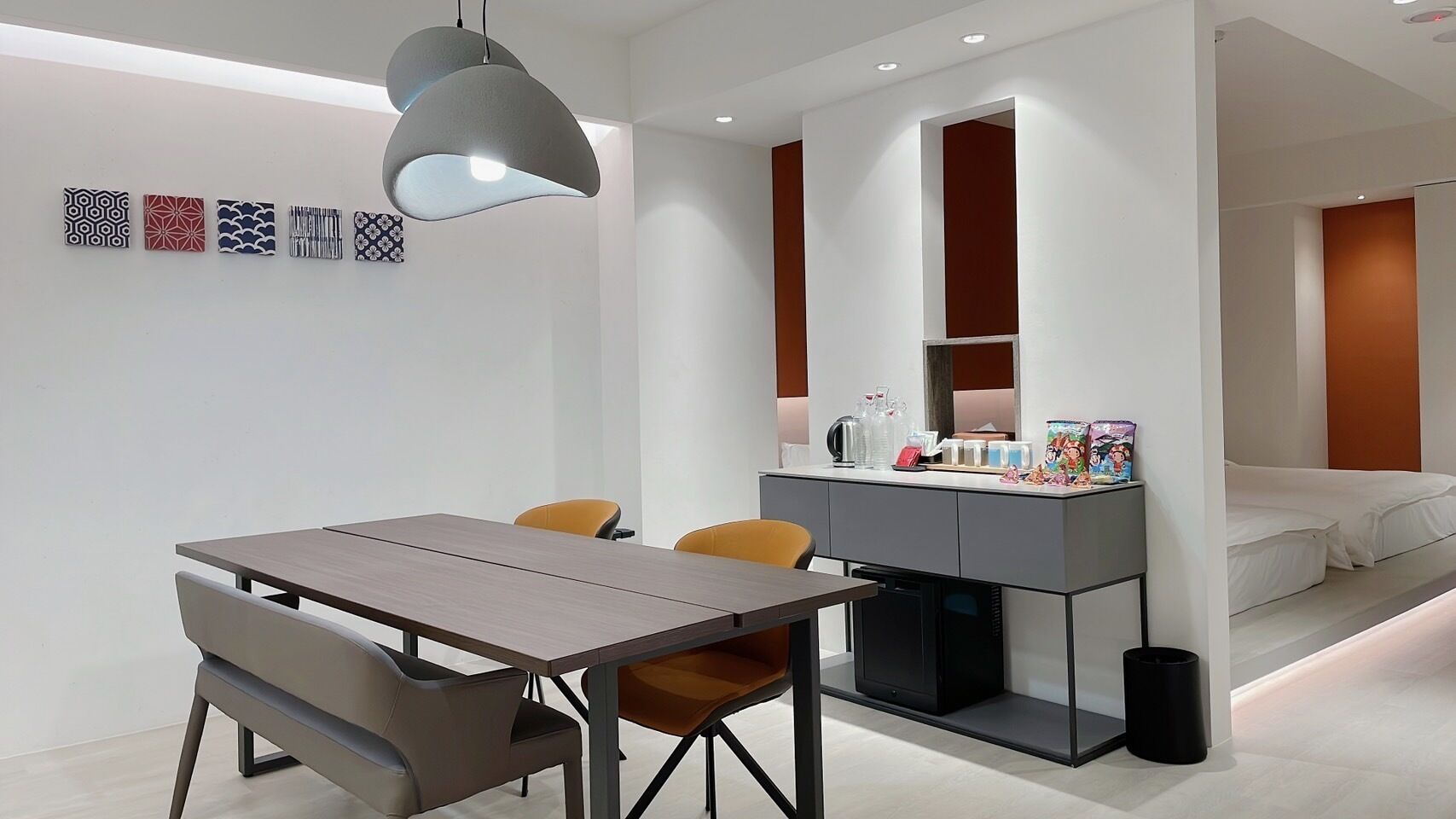 A modern room with a dining table, chairs, a small kitchenette, and a bed.