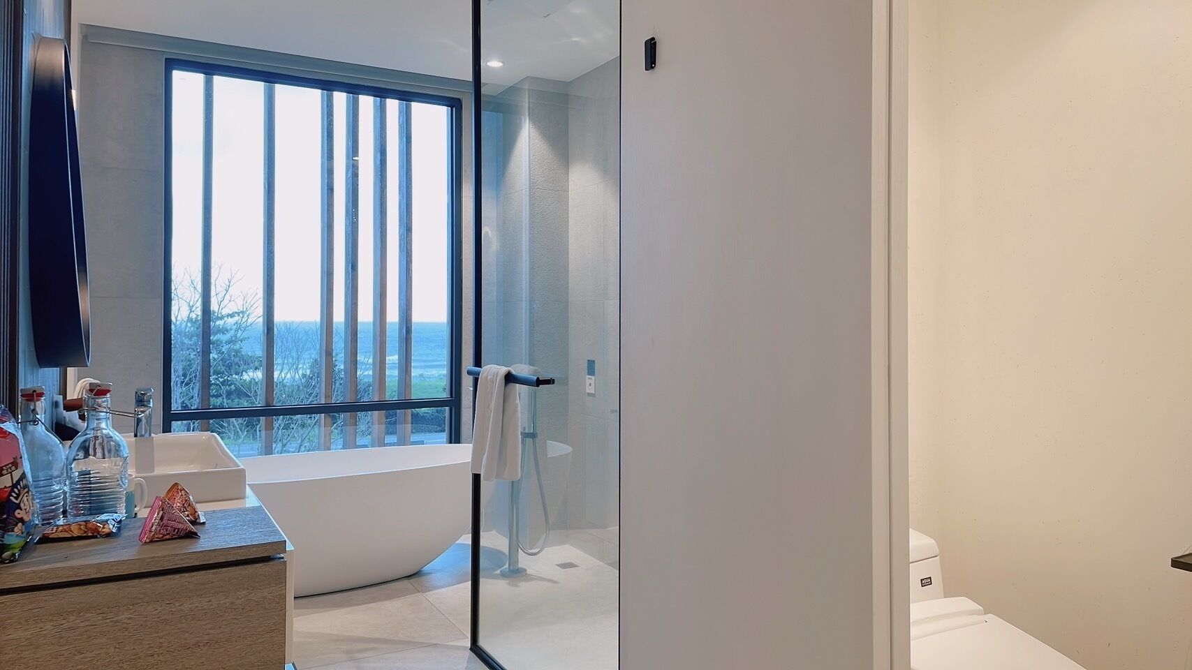 A modern bathroom with a bathtub, a glass shower enclosure, and a large window offering a view of the outdoors.