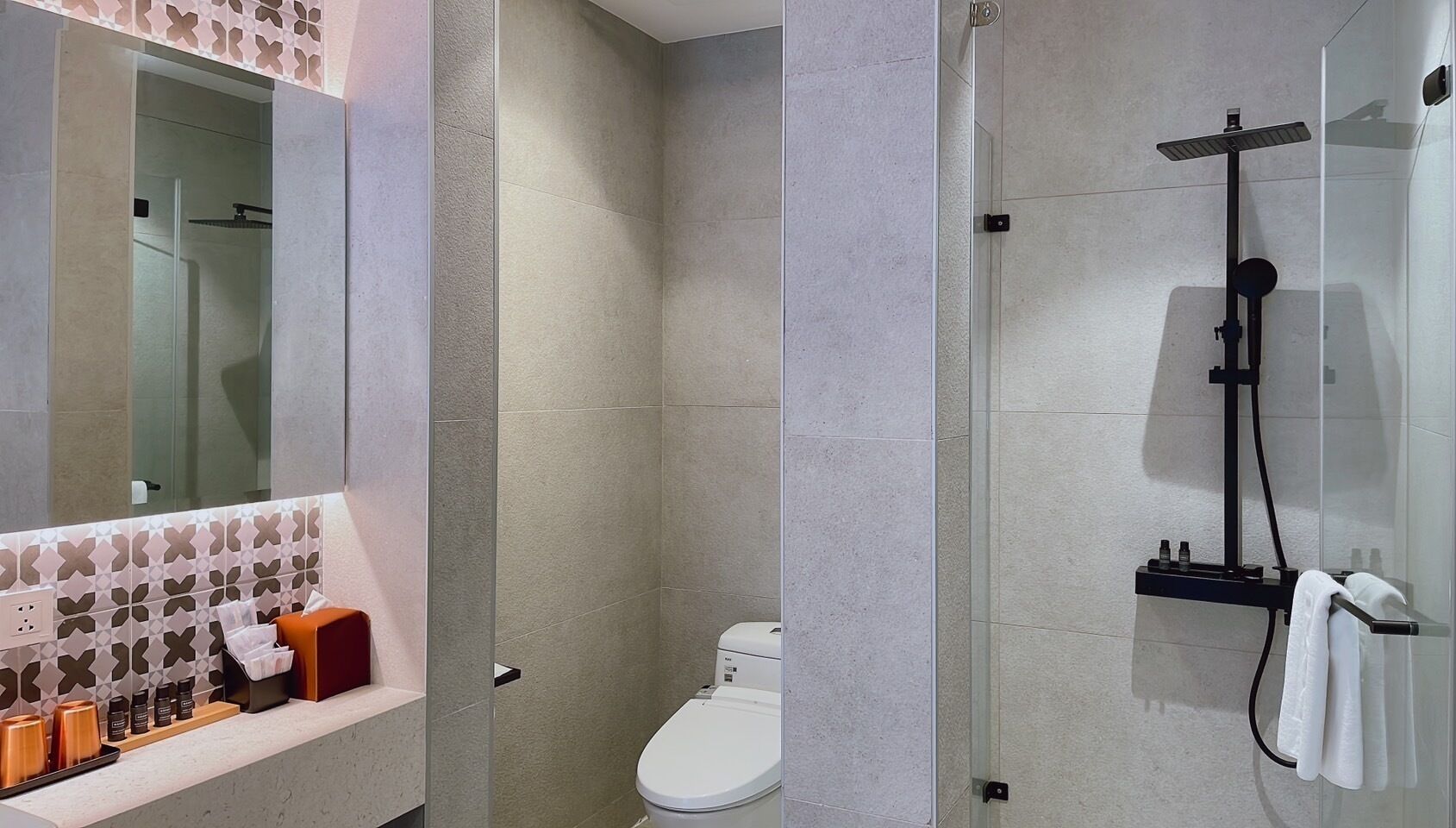 A modern bathroom with a toilet, shower, and a vanity with toiletries.