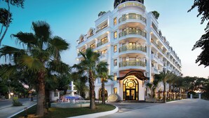 A multi-story hotel with a grand entrance, palm trees, and a fountain. - Grand Sunrise Palace Hoi An (Da Nang)