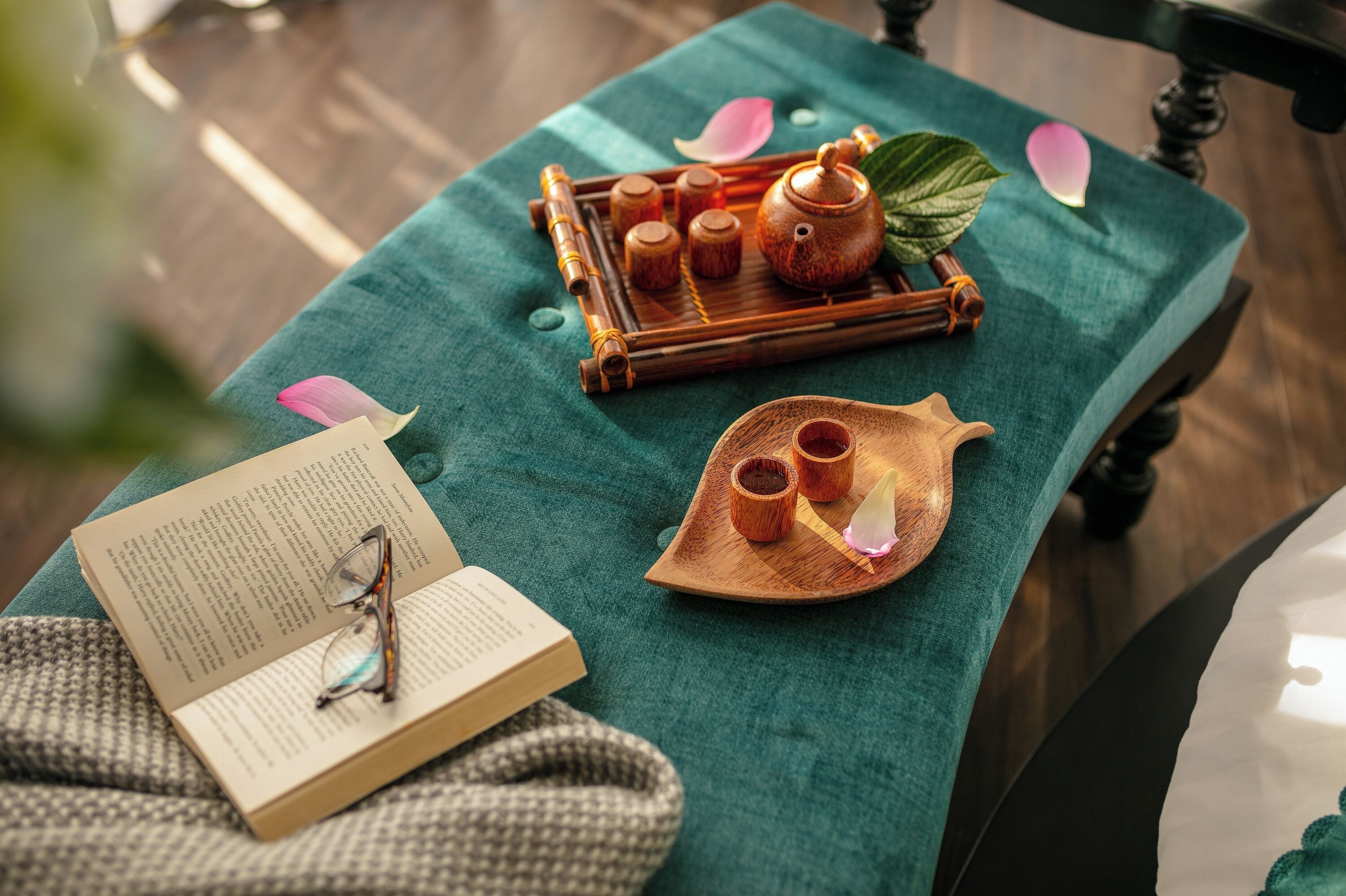 Una mesa con un libro, gafas, y una bandeja con teteras y tazas.