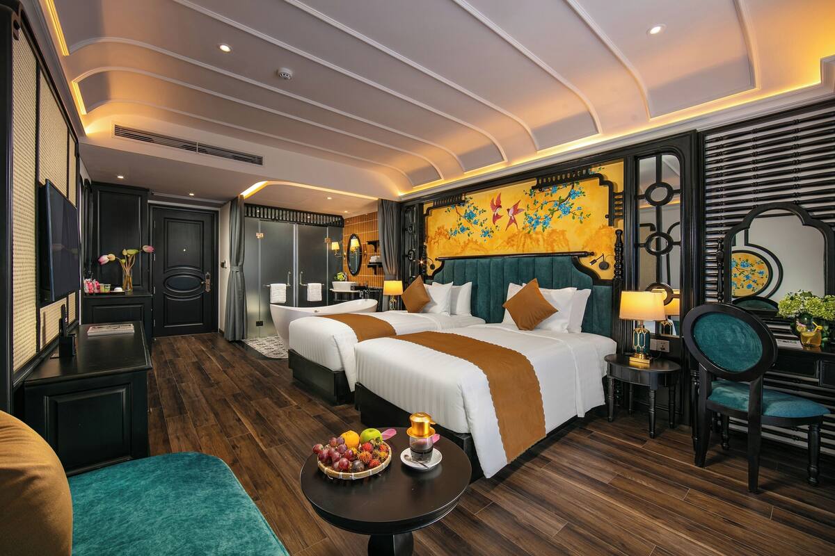 Une chambre d’hôtel avec deux lits, une table à manger avec des fruits, une télévision et une salle de bain avec une baignoire.