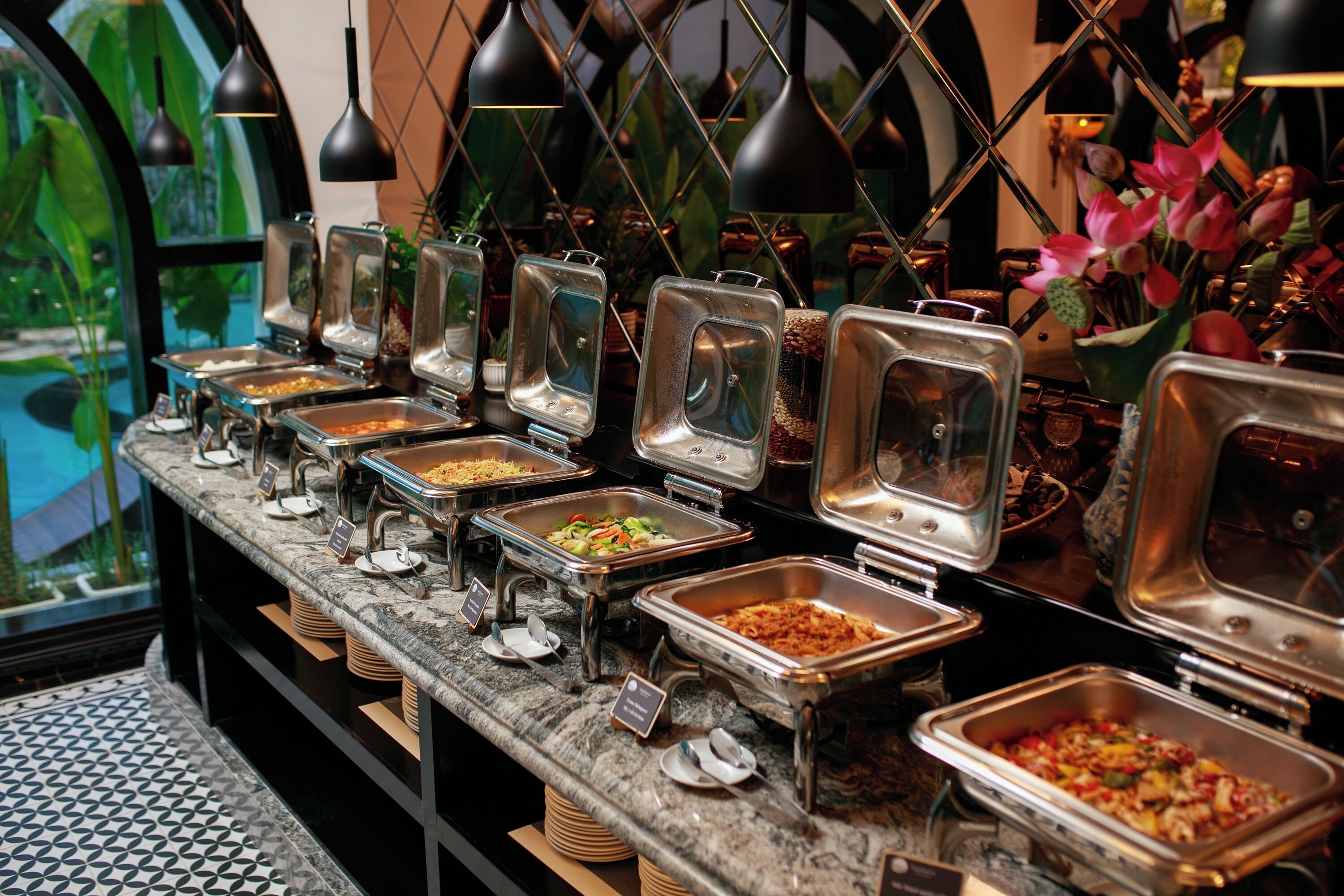 A buffet with various food options, arranged on a marble counter with metal serving trays.