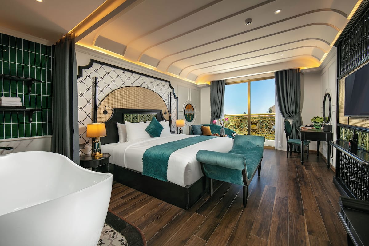 Une chambre spacieuse avec un grand lit, une baignoire et un balcon offrant une vue agréable.