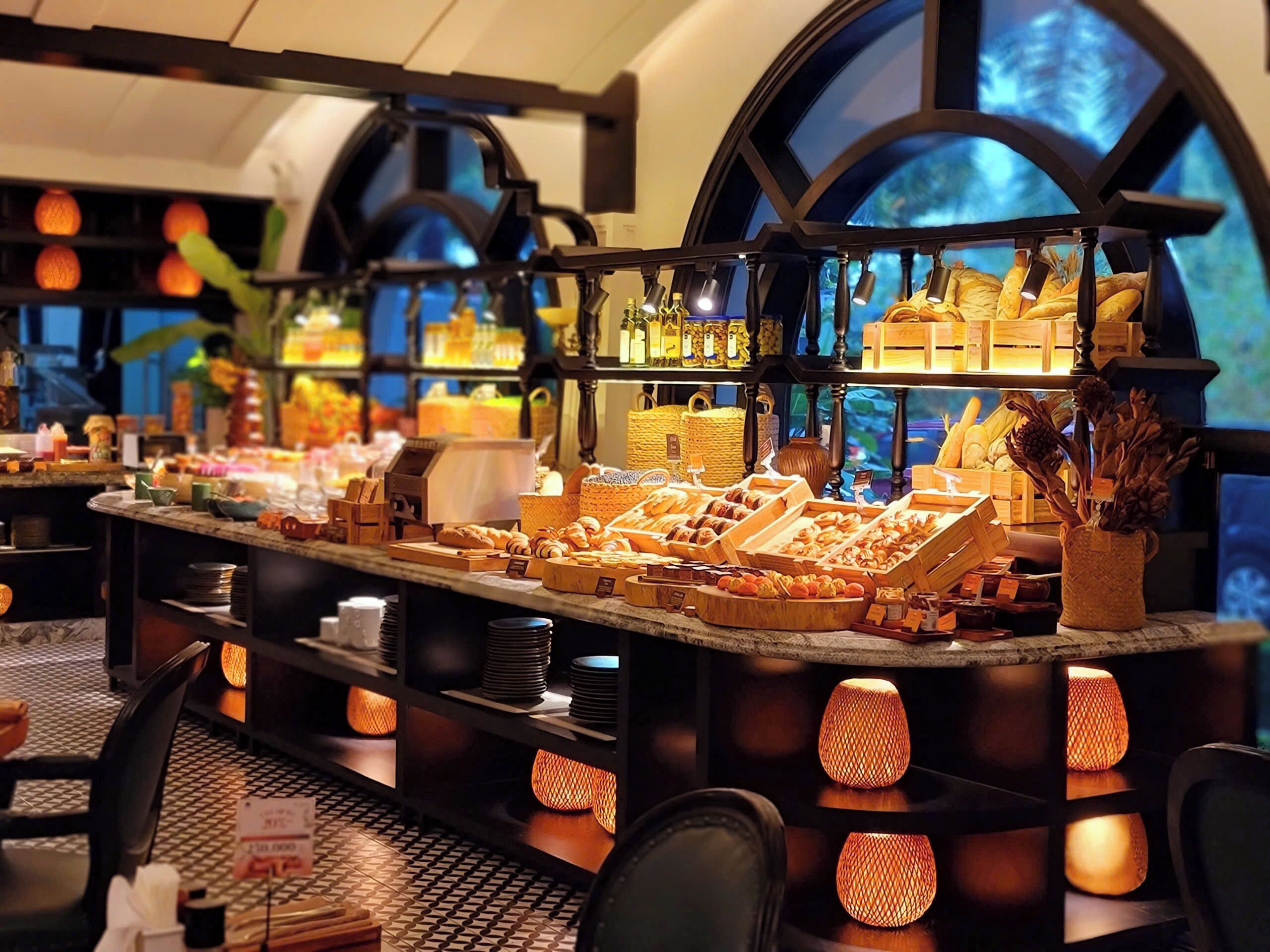 Une vitrine de boulangerie présentant des pâtisseries et du pain, des étagères remplies d’assiettes et un éclairage chaleureux.