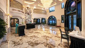 A grand lobby with a marble floor, a reception desk, a chandelier, and a view of the outside through large windows. - Grand Sunrise Palace Hoi An (Da Nang)