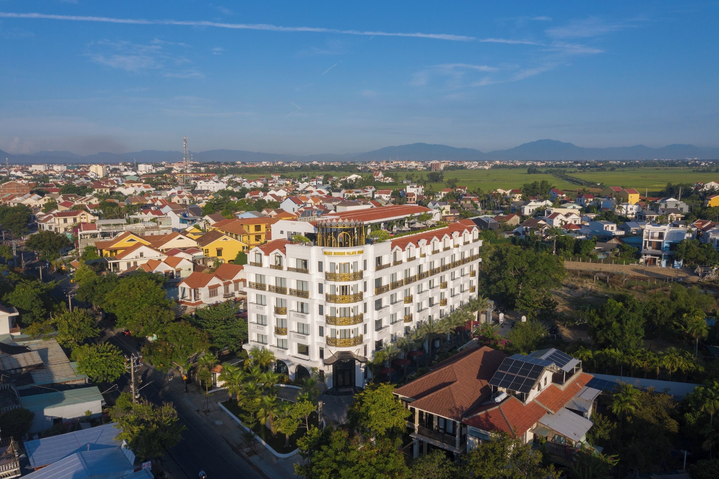 A multi-story hotel with a central courtyard, surrounded by residential buildings and greenery.