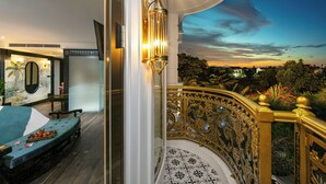 A luxurious bedroom with a large bed, a nightstand, and a mirror. There is a balcony with ornate railings and a view of the cityscape. - Grand Sunrise Palace Hoi An (Da Nang)
