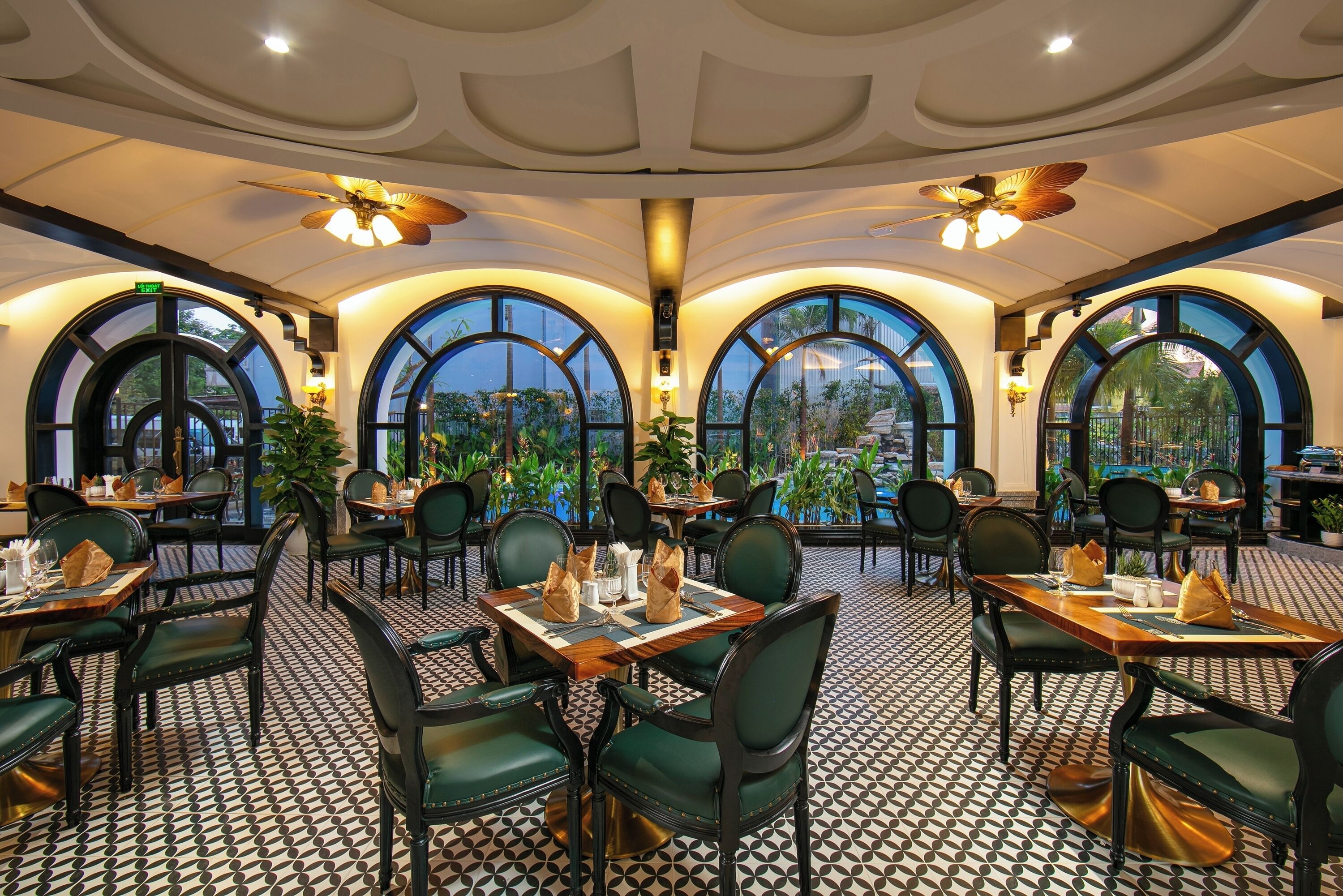 A restaurant with round tables, green chairs, and a patterned floor.