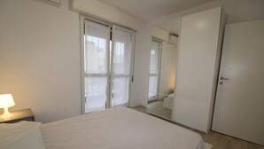 A bedroom with a bed, a nightstand, a mirror, and a wardrobe. - Alideco - Lignano Sabbiadoro (Lignano Sabbiadoro)