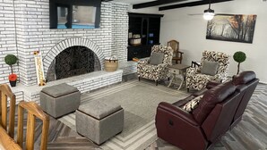 A modern living room with a fireplace, patterned armchairs, a leather sofa, and a herringbone wood floor. - Our Pool House (Lubbock)