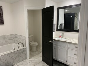 Ein Badezimmer mit Toilette, einer schwarzen Tür, einem weißen Waschbecken mit Marmorplatte und einem Spiegel über dem Waschbecken.