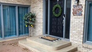 A brick building with a black door, a welcome sign, and a small tree with yellow flowers. - Our Pool House - Swim Rain or Shine (Lubbock)
