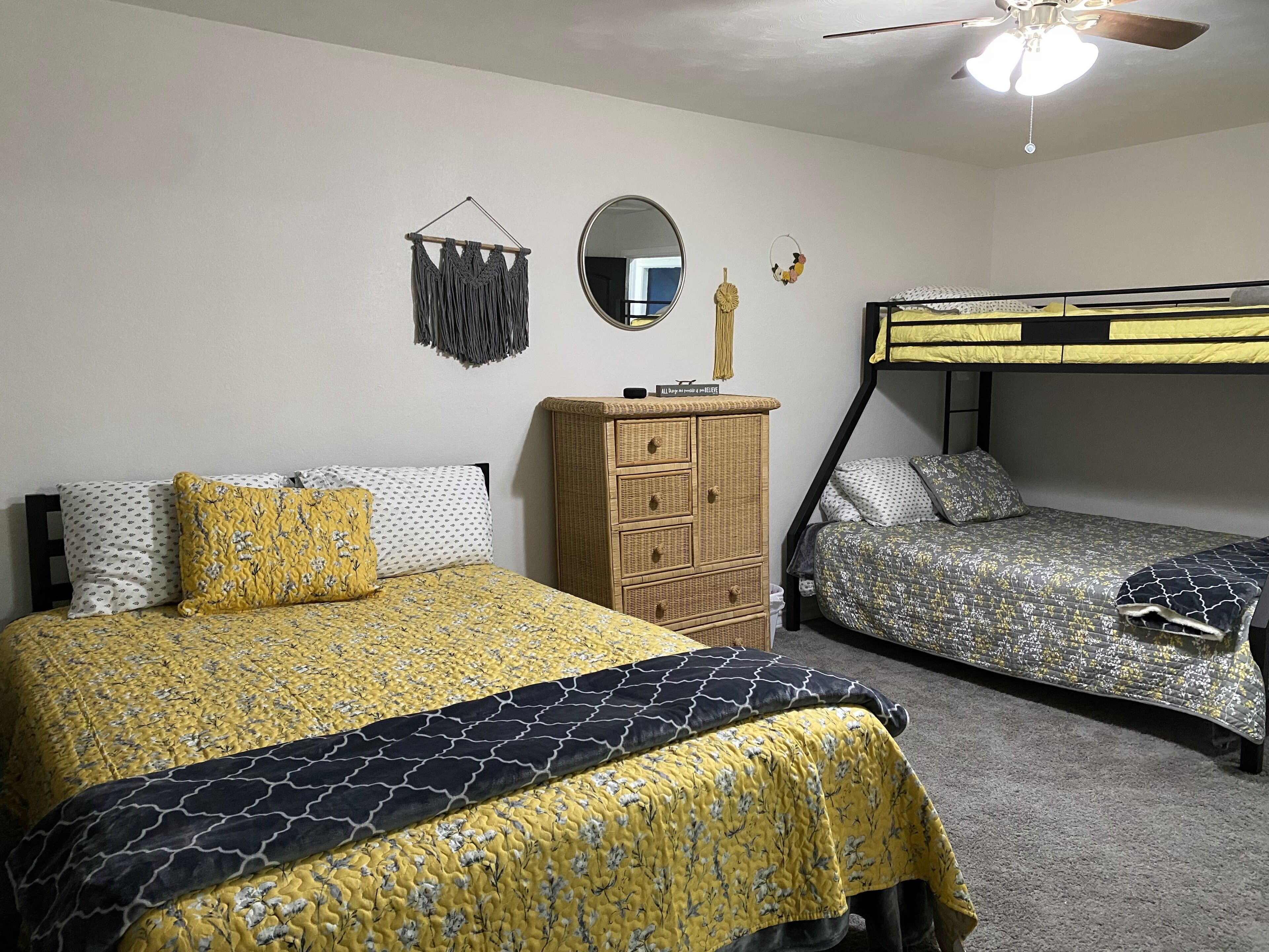 Une chambre avec deux lits, une commode, un miroir et un ventilateur de plafond.